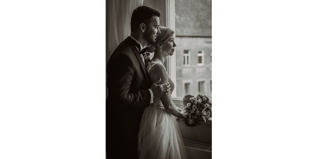 Hochzeitsfotos - Weimar (Weimar, Stadt) - Im sanften Licht des Fensters des Ritterguts Ermlitz habe ich dieses stimmungsvolle Foto vom Bräutigam und der Braut eingefangen. Sie stehen nebeneinander, blicken nachdenklich in die Ferne. Der Bräutigam umarmt die Braut von hinten, eine Geste der Unterstützung und Zuneigung. Die Braut, mit ihrem eleganten Kleid und einem Strauß voller tiefblauer und cremefarbener Blumen, verkörpert die Anmut des Moments. Ihre Gesichter sind von einer ruhigen Vorfreude geprägt, als würden sie gemeinsam in ihre gemeinsame Zukunft schauen. Dieses Bild spiegelt die Intimität und das besondere Ambiente ihres Hochzeitstages wieder. - Mariana Siegert