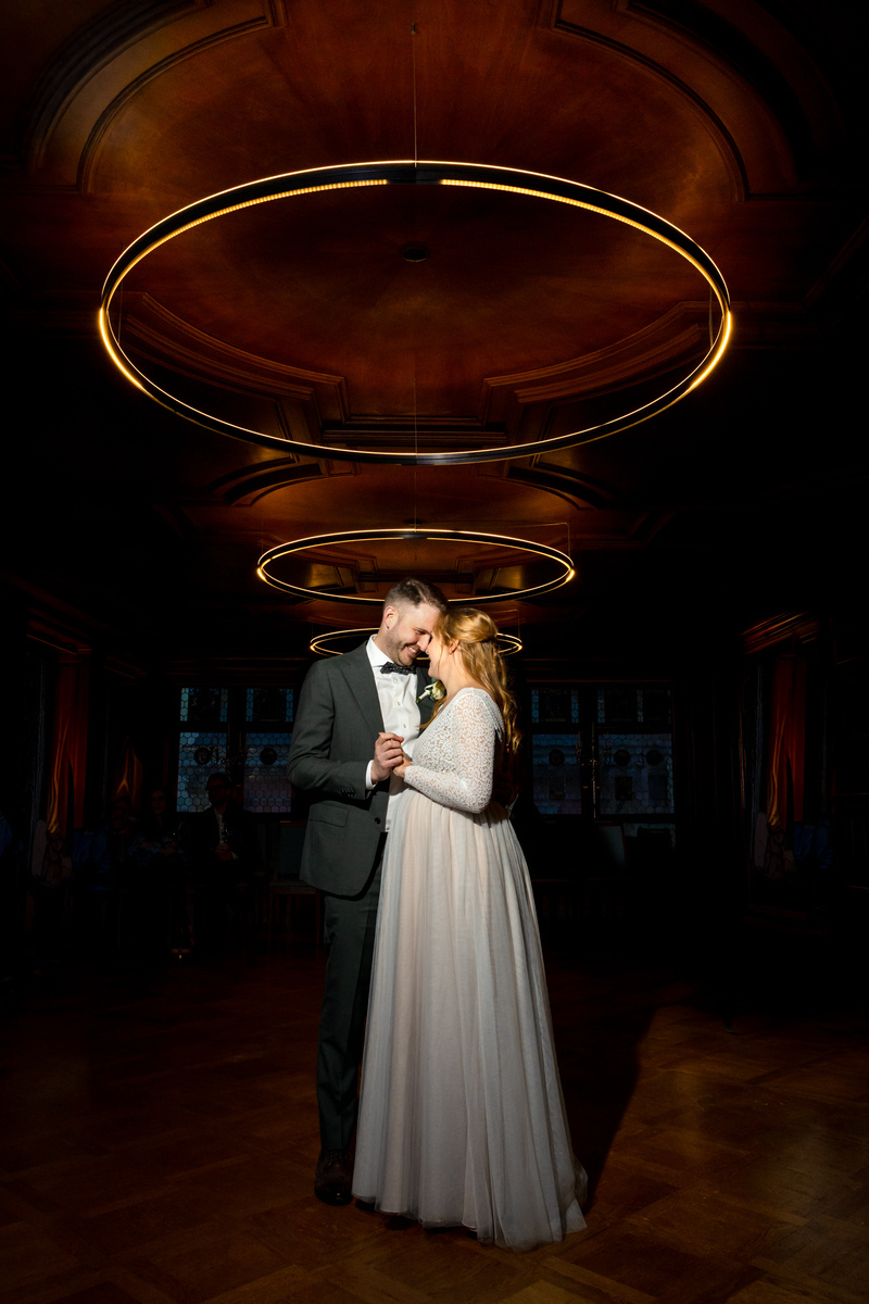 Hochzeitsfotos - Art des Shootings: Hochzeits Shooting - Feldbach (Hombrechtikon) - Brautpaar steht eng umarmt im Zunfthaus zur Waag in Zürich nach der zivilen Hochzeit mit warmem Licht und Ringlampen an der Decke - Mischa Bättig