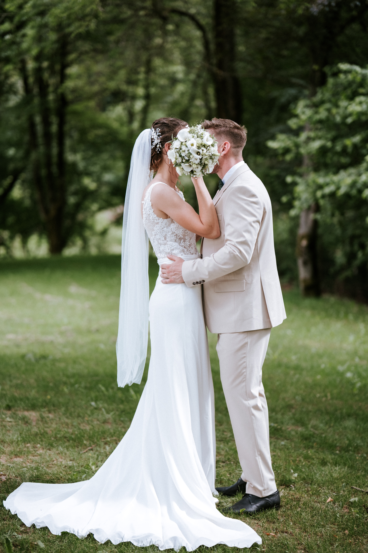 Hochzeitsfotograf: Brautpaar küsst sich hinter dem Brautstrauß, Paarfotos im Grünen am Kahlenberg in Wien - Pengoo Weddings