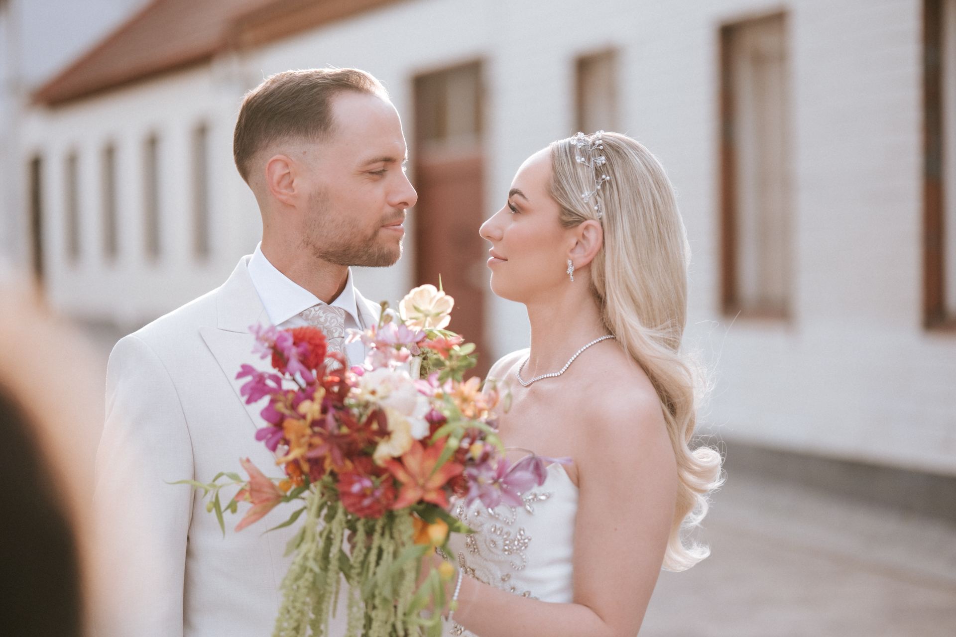 Hochzeitsfotograf: Brautpaar sieht sich verliebt an, Braut mit buntem Brautstrauß beim Alten Rathaus Wiener Neudorf - Pengoo Weddings
