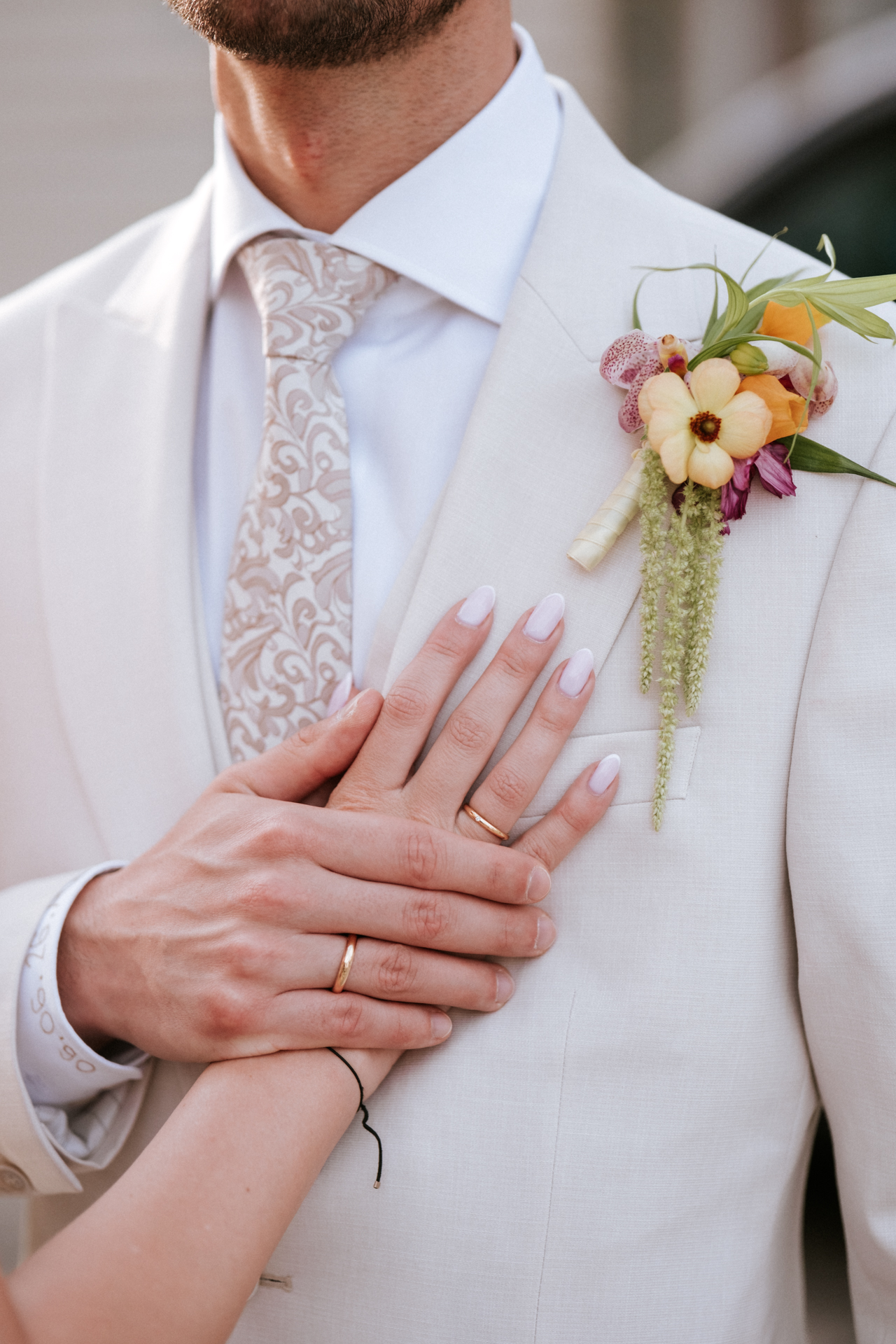 Hochzeitsfotograf: Hand der Braut mit Ehering auf der Brust des Bräutigams, Detail mit Anstecker, Wiener Neudorf - Pengoo Weddings