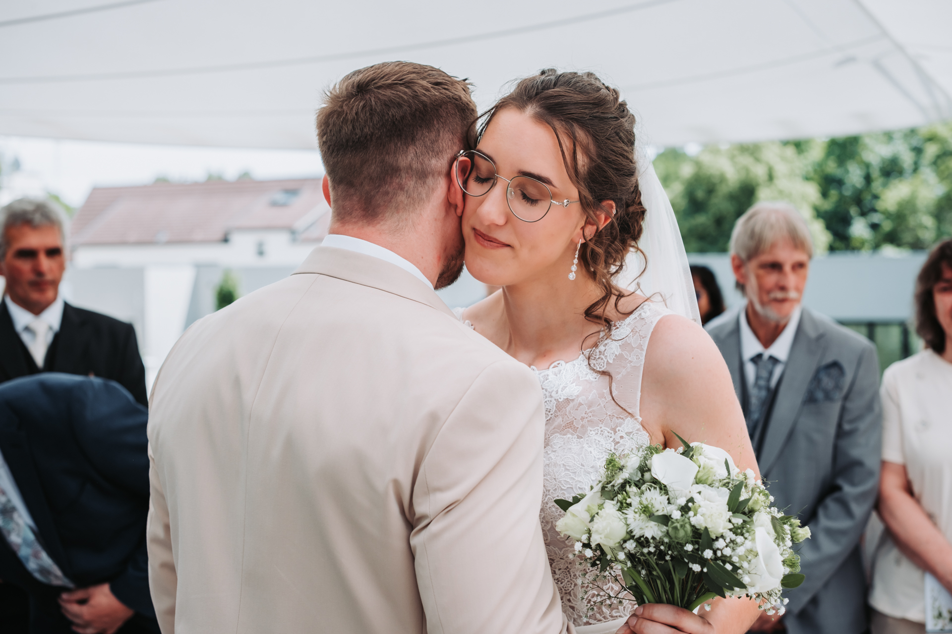 Hochzeitsfotograf: Brautpaar umarmt sich nach der Trauung, Gäste im Hintergrund, Schönstatt-Kapelle am Kahlenberg in Wien - Pengoo Weddings