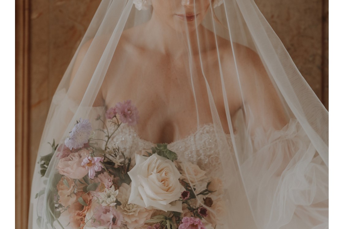 Hochzeitsfotograf: Ein wundervolles Portrait von einer Braut mit einem einzigartigen Schleier. Sie hält einen farbenfrohen Brautstrauss in den Händen und lässt sich von der Fotografin aus Berlin, Maria, in der Normandie, in einem Schloss ablichten. - Lensofbeauty